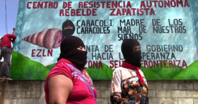 Dos zapatistas frente a un cartel que reza "Centro de resistencia autonoma rebelde zapatista"