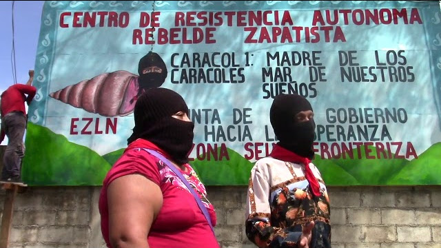 Dos zapatistas frente a un cartel que reza "Centro de resistencia autonoma rebelde zapatista"